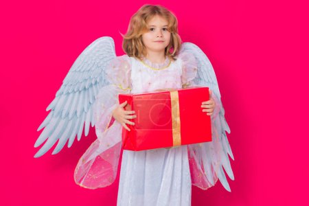 Foto de Linda niña ángel con regalo caja regalo. Ángel niño. Retrato de niño lindo con alas de ángel aislado en el fondo del estudio. angelito, día de San Valentín. Niños angelicales - Imagen libre de derechos