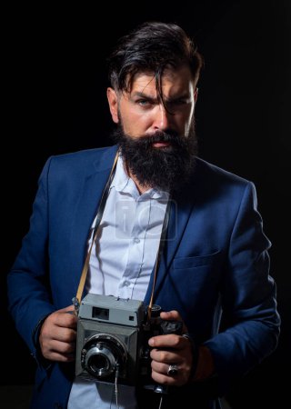 Téléchargez les photos : Photographe professionnel. Portrait d'un photographe homme sérieux avec un vieil appareil photo vintage rétro isolé sur fond noir - en image libre de droit