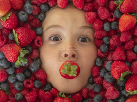 Téléchargez les photos : Bannière Berry. Les enfants font face avec des fruits et des baies. Fraise d'été, myrtille, framboise, fond de mûre. Vue du dessus photo du visage de l'enfant en arrière-plan de baies. Enfants en bonne santé manger - en image libre de droit
