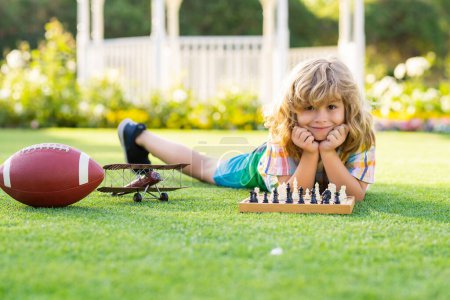Photo for Dream kids and childhood concept. Child playing chess game in spring backyard, laying on grass. Concentrated kid play chess. Kid playing board game outdoor - Royalty Free Image