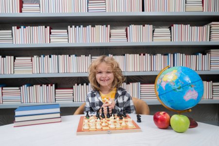 Foto de Un niño juega al ajedrez en la escuela. Inteligente niño concentrado y pensante jugando ajedrez. Niño niño desarrollando estrategia de ajedrez, juego de mesa - Imagen libre de derechos