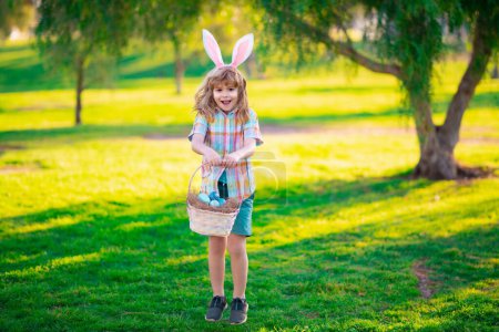 Foto de Niños en orejas de conejo en la búsqueda de huevos de Pascua en el jardín. Niños con huevos de colores en el parque. Feliz Pascua - Imagen libre de derechos