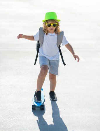 Foto de Niño montando monopatín en la carretera. Kid practicando skate. Los niños aprenden a andar en monopatín en un parque el soleado día de verano. Niño patinando en monopatín - Imagen libre de derechos