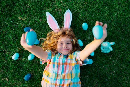 Child with rabbit ears, Easter holidays. Kid hunting Easter eggs. Cute bunny boy, funny kids portrait. Top view funny kids face
