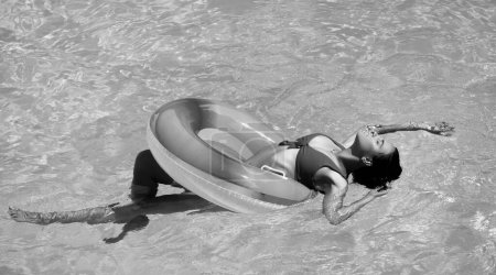 Téléchargez les photos : Vacances d'été. Profitant du bronzage. Femme en maillot de bain sur cercle gonflable dans la piscine - en image libre de droit