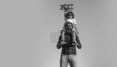 Photo for Father and son playing with wooden airplane. Boy sitting on fathers shoulders - Royalty Free Image
