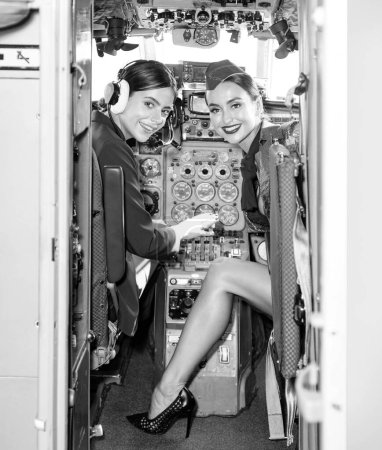 Téléchargez les photos : Pilote et instructrice de vol dans le poste de pilotage d'un aéronef. Belles jeunes femmes souriantes pilotes assis dans la cabine de l'avion. Portrait de jolie jeune femme pilote avec casque - en image libre de droit