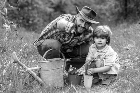 Foto de Padre e hijo de jardinería. Pequeño hijo ayudando a su padre a plantar el árbol mientras trabajan juntos en el jardín - Imagen libre de derechos
