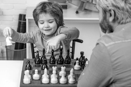 Foto de Padre enseñando hijo. Niño alegre sentado en la mesa y mostrando alegría mientras juega al ajedrez - Imagen libre de derechos