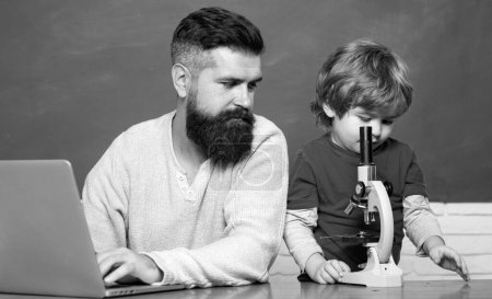 Photo for Teacher helping pupils studying on desks in classroom. Young boy doing his school homework with his father. Chalkboard background. Dad son are concentrated on the problem - Royalty Free Image