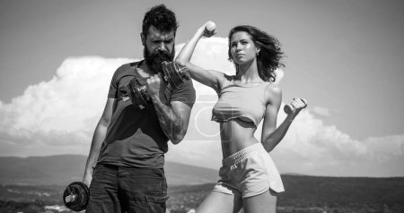 Photo for Strong man and sexy woman working out with dumbbells on sky background. Couple training with dumbbells, athletic sport couple exercise outdoor - Royalty Free Image