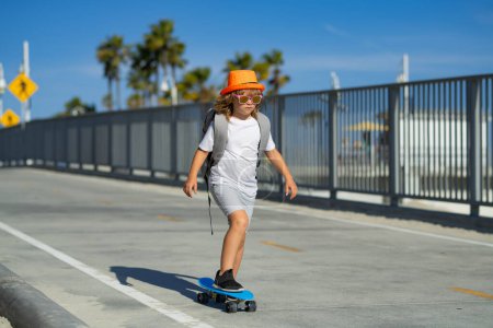 Foto de Niño montando monopatín en la carretera. Kid practicando skate. Los niños aprenden a andar en monopatín en un parque el soleado día de verano. Niño en patineta patinaje - Imagen libre de derechos