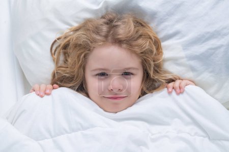 Téléchargez les photos : Enfant au lit avec matelas confortable oreiller doux literie blanche. Couverture de réveil pour enfant. Bonjour. - en image libre de droit