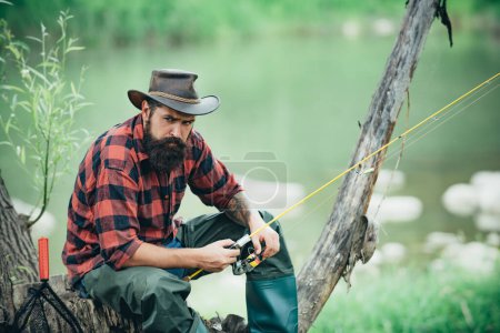 Téléchargez les photos : Jeune homme barbu pêchant dans un lac ou une rivière. Pêche au mouche - en image libre de droit