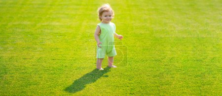 Foto de Bebé en el campo de hierba de primavera, bandera. Bebé parado descalzo en el césped verde. Un niño jugando en el parque de verano. Feliz infancia y cuidado de niños - Imagen libre de derechos