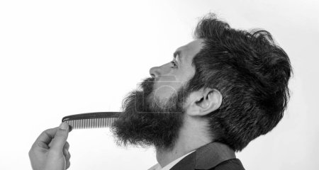 Téléchargez les photos : Homme barbu avec barbe, gay barbu. Concept de salon de coiffure. Des moustaches. Gros plan d'un jeune homme coiffant sa longue barbe avec un peigne - en image libre de droit