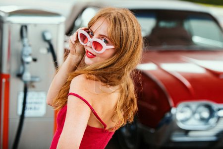 Téléchargez les photos : Voiture rétro rouge. Une vieille voiture américaine. Femme souriante sur la station-service - en image libre de droit