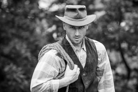 Photo for Western style men fashion. Handsome cowboy in plaid shirt at beautiful rural nature background. Sexy masculine stylish cowboy macho man holding lasso rope - Royalty Free Image