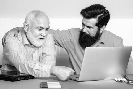 Téléchargez les photos : Un aîné enseigne l'ordinateur portable à son vieux fils. Fils et vieux père utilisant l'ordinateur pour discuter ensemble de nouvelles ou de films - en image libre de droit