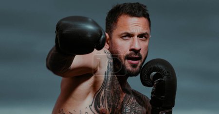 Photo for Boxer in a fight. Fist fight. Strong man with tattooed body boxing outdoor. Man with muscular body and bare torso with boxing punch gloves. Boxing training outside - Royalty Free Image