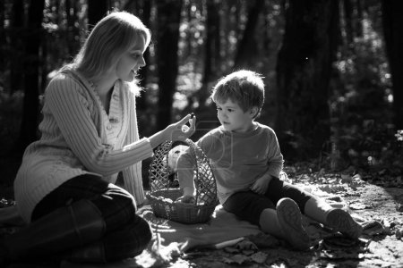 Foto de Joven madre dando a su pequeño hijo una dulce berrie temporada en el picnic de otoño. Mamá y el niño sentados en la manta de picnic y comiendo de la cesta de picnic. Día cálido soleado otoñal. Concepto familiar - Imagen libre de derechos