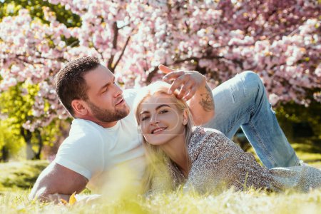 Téléchargez les photos : Joyeux couple de printemps amoureux s'amuser. Deux jeunes gens se relaxant dans des fleurs de sakura. Amateurs souriants se relaxant dans le parc. Famille sur fond de fleurs de la nature. Relations et rencontres - en image libre de droit