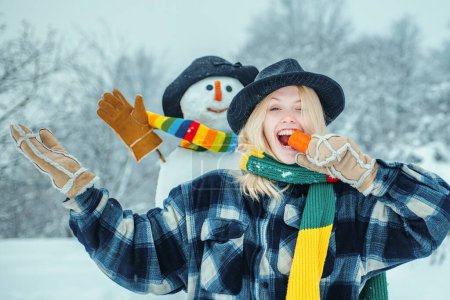 Foto de Muñeco de nieve con nariz de zanahoria divertida con chica divertida. Retrato de moda de una joven modelo en el interior con muñeco de nieve de Navidad. Preparación de Navidad - chica divertida hacer muñeco de nieve - Imagen libre de derechos