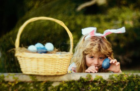 Foto de Child with rabbit ears, Easter holidays. Kid hunting Easter eggs in easters basket. Cute bunny boy, funny kids portrait - Imagen libre de derechos