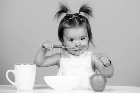 Foto de Bebé comiendo comida para niños. Niño comiendo comida saludable con una cuchara en el estudio, aislado. Cara divertida de los niños - Imagen libre de derechos