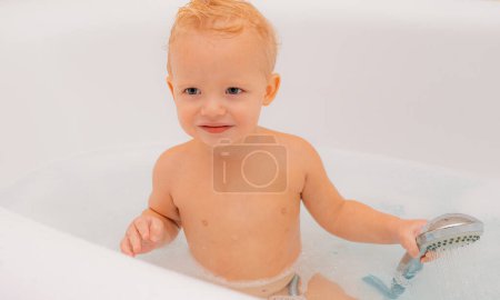 Téléchargez les photos : Bain moussant. Petit lavage de bébé avec des bulles. Salle de bains. Petit enfant prenant un bain avec mousse et se lavant la tête et souriant - en image libre de droit