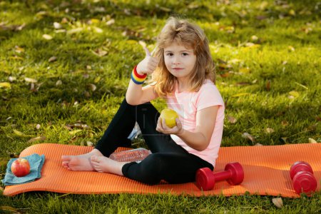 Photo for Sport kids boy. Healthy lifestyle and healthy food concept. Little boy child in sportswear eating apple sitting on sport mat after training on sunny spring day - Royalty Free Image