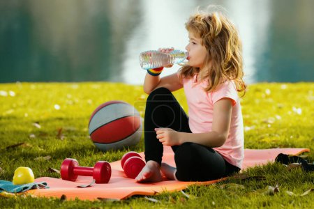 Photo for Child boy drink water relax on sport mat after sport exercises outdoor in park. Concept of children sport - Royalty Free Image