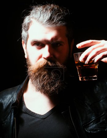 Foto de Man drinking whiskey, brandy, cognac. Man with glass of brandy. Bearded hipster with glass of whiskey. Old traditional whiskey drink - gentlemans beverage. Barman serves cognac - Imagen libre de derechos