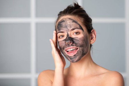 Gesichtsbehandlung. Schöne junge Frau mit Kohleschlamm Gesichtsmaske auf dem Gesicht. Hautpflege und -behandlung. Gesichtsmaske aus schwarzem Ton