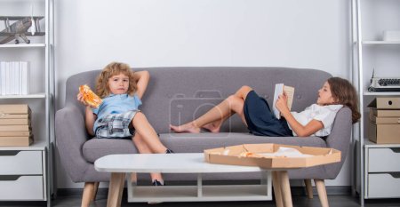 Photo for Home kids leisure. Entertainment for children. Kids eating pizza reading book enjoying leisure at home. Two little children relaxing at home. Children friends spend leisure together in living room - Royalty Free Image