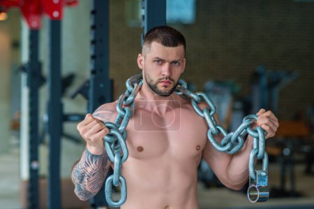 Photo for Sexy muscular man pumps his muscles and lifts weight sport metal chain in gym. Strong fit man exercising with chains. Muscular young handsome man lifting weights. Weightlifting and training - Royalty Free Image