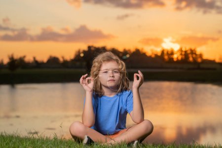 Photo for Kid calmness and relax on nature background. Little kid meditates while practicing yoga. Freedom and carefree concept. Outdoors meditating in summer sunset - Royalty Free Image