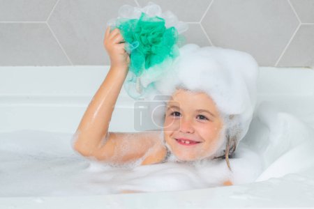 Téléchargez les photos : Garçon enfant dans un bain avec mousse. Procédures de baignade et d'hygiène pour enfants - en image libre de droit