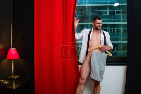 Photo for Fashion look, fashionable suit for business man. Man standing near window. Seductive gay. Muscular body of man in hotel room. Sexy guy with naked body. Nude muscular man body with tattoo - Royalty Free Image