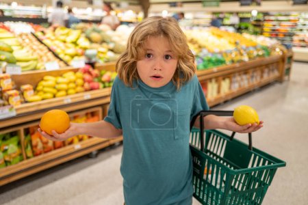 Téléchargez les photos : Enfant avec citron et orange. Petit enfant choisissant de la nourriture dans une épicerie ou un supermarché - en image libre de droit