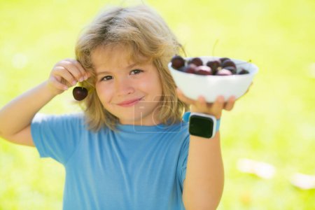 Téléchargez les photos : Face d'enfant d'été. Les enfants mangent des cerises en été. Le gamin cueille des cerises dans le jardin - en image libre de droit