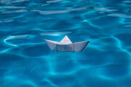 Foto de Nave de origami. Barco de papel sobre el fondo del mar. Origami barco de papel navegando en el agua causando olas y ondas - Imagen libre de derechos