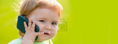 Photo for Baby on spring grass field, banner. Cute baby face closeup on green grass in summertime. Funny little kid portrait with mobile phone, smartphone on nature. Happy Childhood - Royalty Free Image