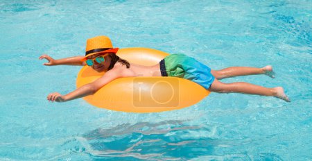Foto de Sonriente niña linda en gafas de sol y sombrero de verano en la piscina en el día soleado. Salpicaduras de niños y nadar en la piscina. Nadar actividad deportiva acuática en vacaciones de verano con niños - Imagen libre de derechos