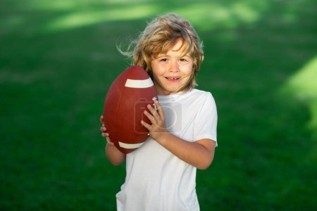 Téléchargez les photos : Enfant sportif. Enfant avec football américain, ballon de rugby. Portrait mignon d'un footballeur américain, extérieur - en image libre de droit