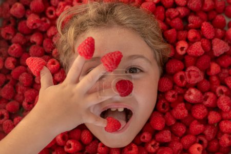 Photo for The kids face with raspberries fruit and berries. Summer, pink red raspberry background - Royalty Free Image