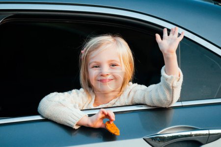 Téléchargez les photos : Une petite fille sort sa tête par la fenêtre de la voiture. Road trip ou concept de voyage. Les enfants heureux voyagent en voiture. Mignon enfant appuyé par la fenêtre d'un van, souriant et agitant - en image libre de droit