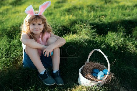 Téléchargez les photos : Enfant mignon avec panier de Pâques sur l'herbe. Enfant chassant des œufs de Pâques. Enfant mignon en costume de lapin avec des oreilles de lapin ayant Pâques - en image libre de droit