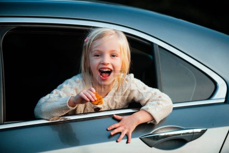 Téléchargez les photos : Petite fille excitée admirant les regards de la voiture dans la rue. Mignon petit enfant fille souriant et amusant de voyager en voiture - en image libre de droit
