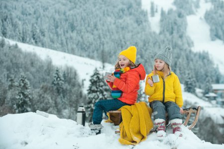 Photo for Kids on Picnic in winter. Little couple sitting on sled in snow drinking hot tea, enyoying holiday season. Winter camping - Royalty Free Image